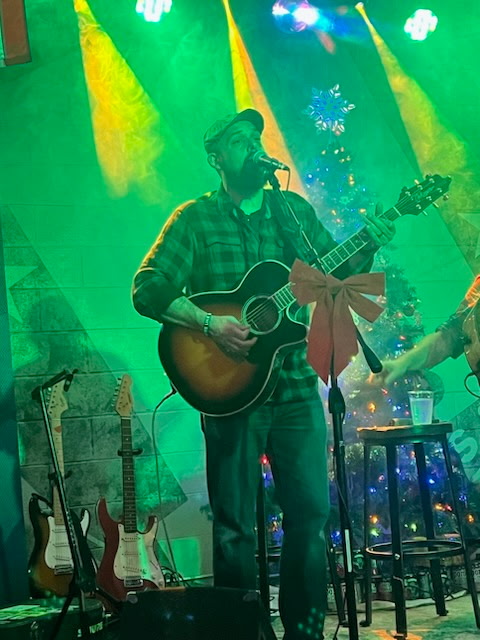 Scott Womack performing acoustic guitar under green stage lights